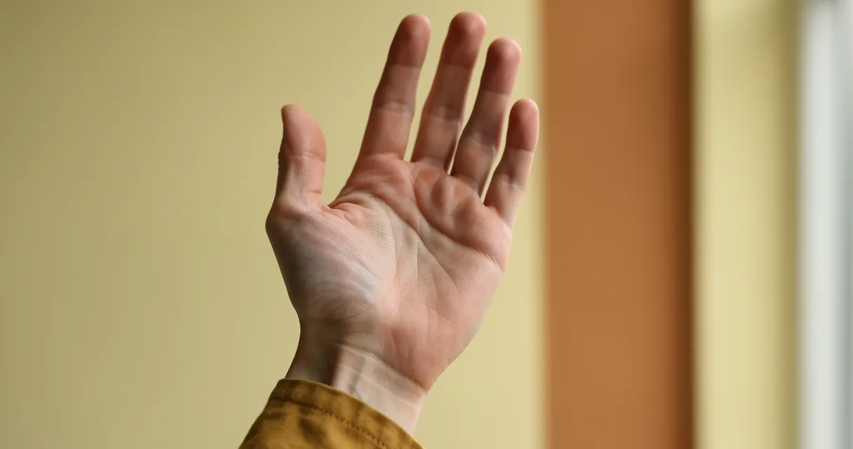 An open palm in window light against a pale yellow wall